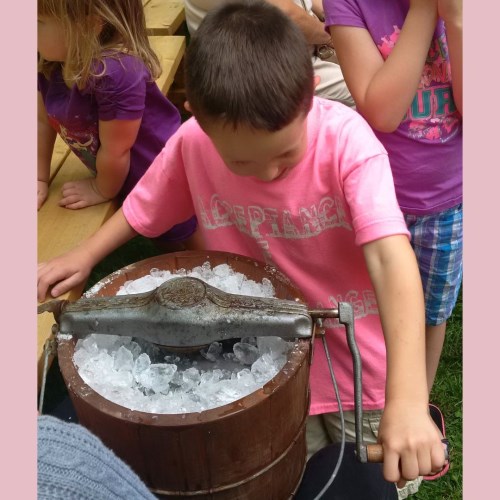 Image of child with pink shirt using a crank churn to make ice cream 