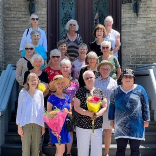 Image of volunteers on front steps at Glanmore. It is summer and some are holding bouquets of flowers.