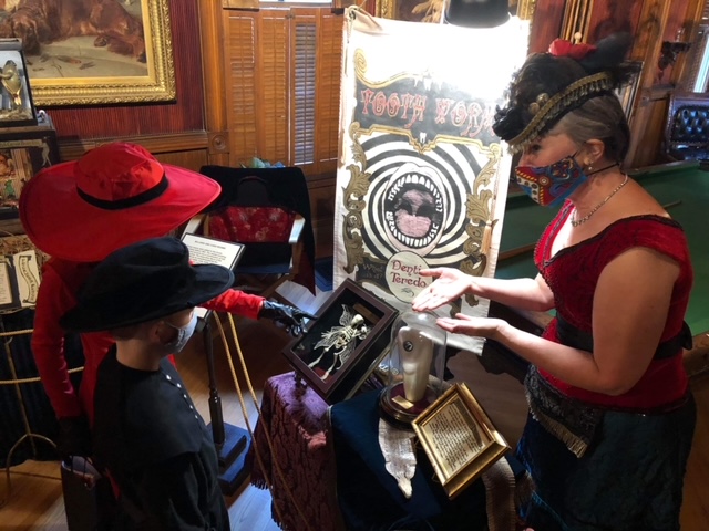 children in costume interacting with a woman in Victorian clothing as part of a sideshow for Halloween event