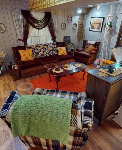 Image of 1973 living room vignette with a brown couch with orange floral accent pillows and a granny square crocheted afghan blanket