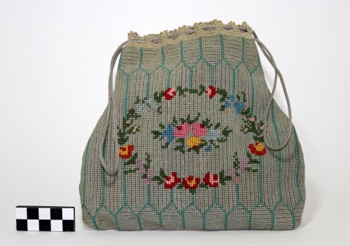 A green reticule, small drawstring bag, embellished with a circular floral pattern.