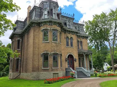 The exterior facade of Glanmore National Historic Site, a second empire style-residence. The circular driveway and a flowerbed are in front of the house. 