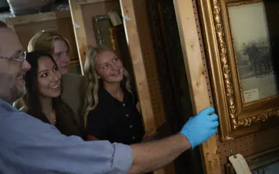 A man wearing latex gloves shows a group of people paintings in Glanmore National Historic Site's artifact storage.