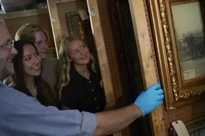 A man wearing latex gloves shows a group of people paintings in Glanmore National Historic Site's artifact storage.
