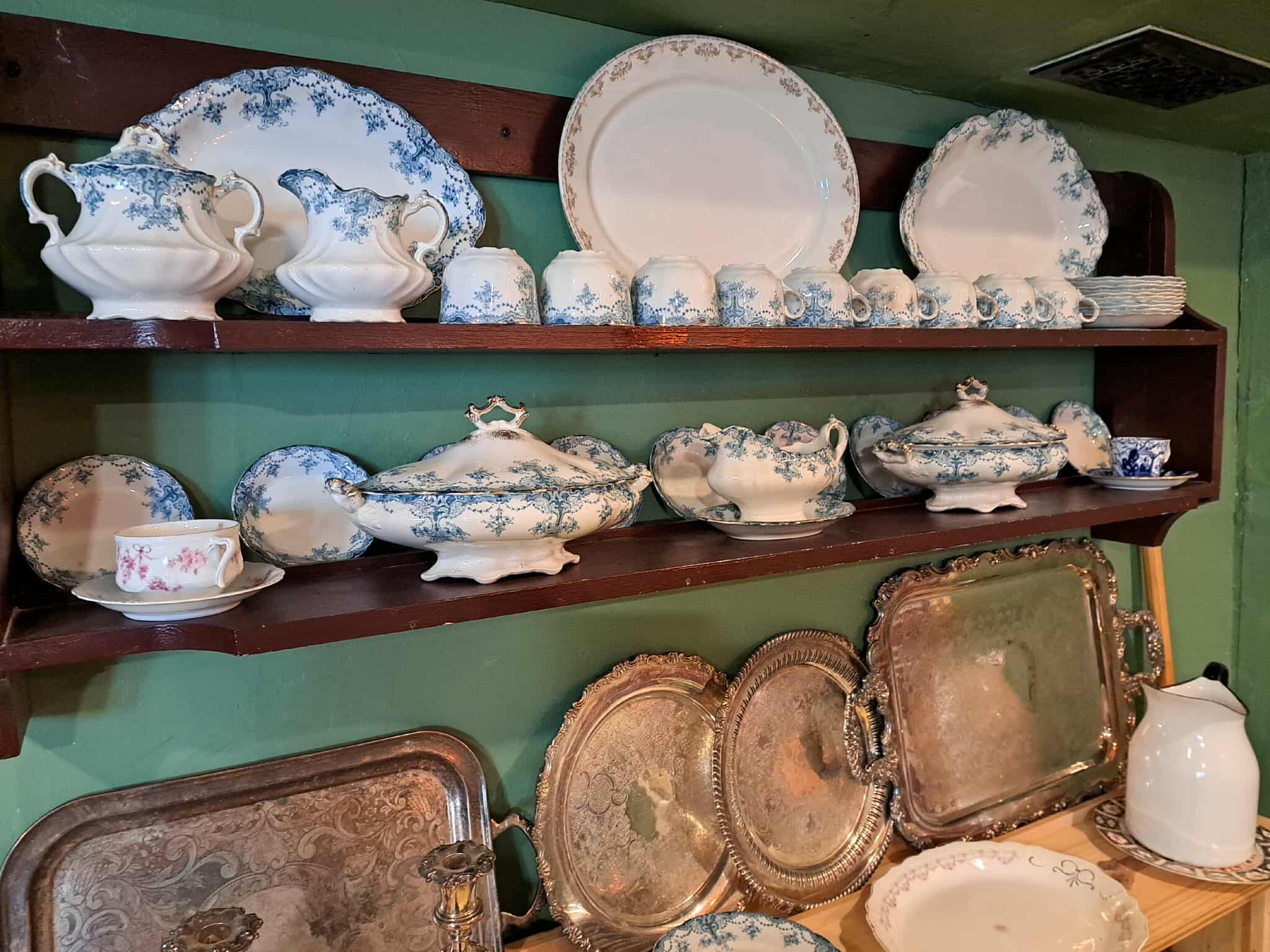 A collection of white and blue dishes and silver platters displayed on shelves in Glanmore's kitchen exhibit.