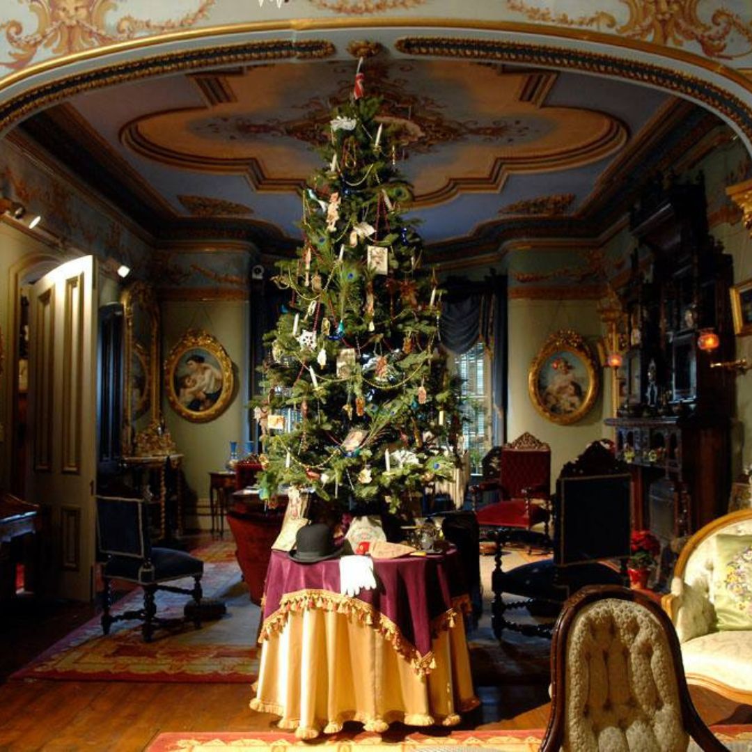 A christmas tree stands on a table in the centre of a large elaborately decorated room. 