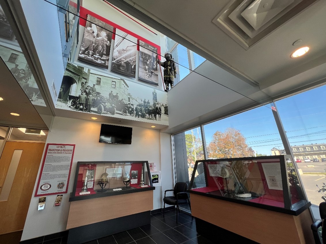 Display cases and a mural of a historic photograph with a mannequin dressed as a firefighter. Part of the exhibition entitled, Loyalty, Tradition and Progress which features the history of fire fighting in Belleville and is on display at Belleville's Fire and Emergency Services Headquarters