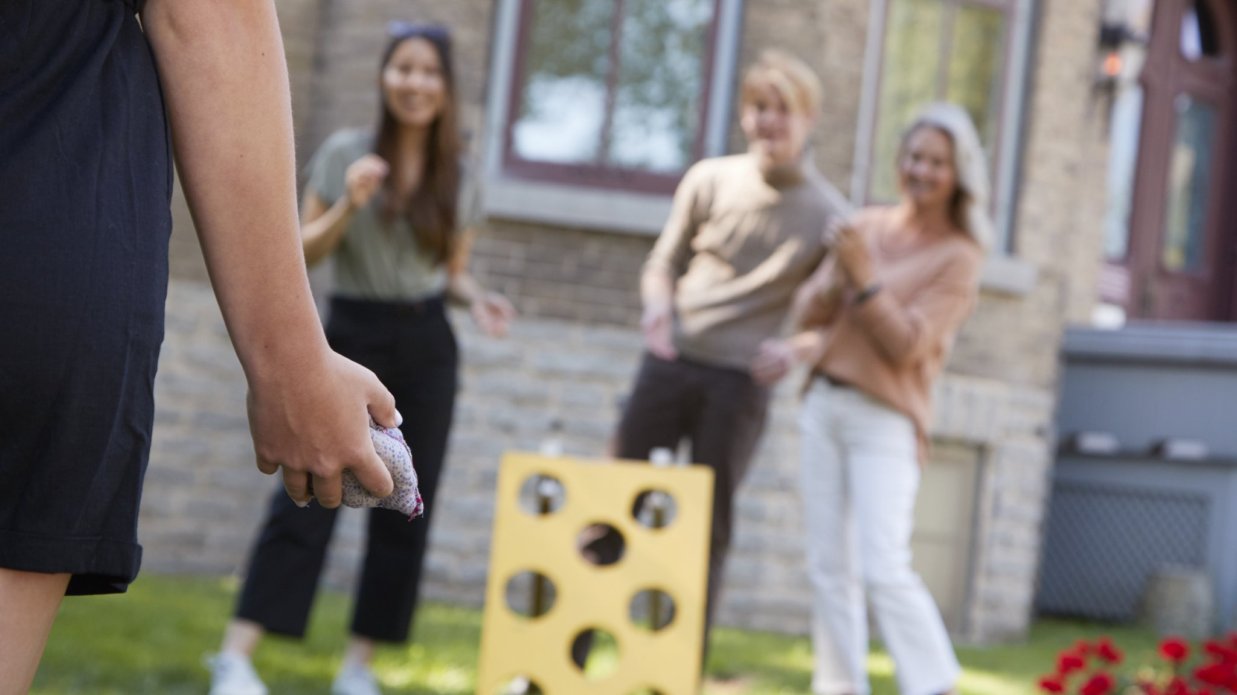 A group of adults play old-fashioned bean bag toss on the lawn outside Glanmore. The target board is bright yellow. 