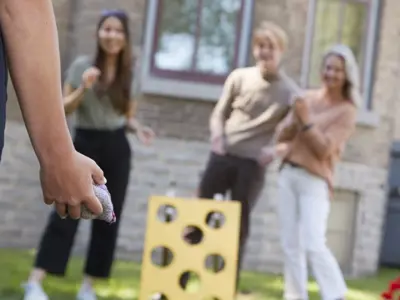A group of adults play old-fashioned bean bag toss on the lawn outside Glanmore. The target board is bright yellow. 