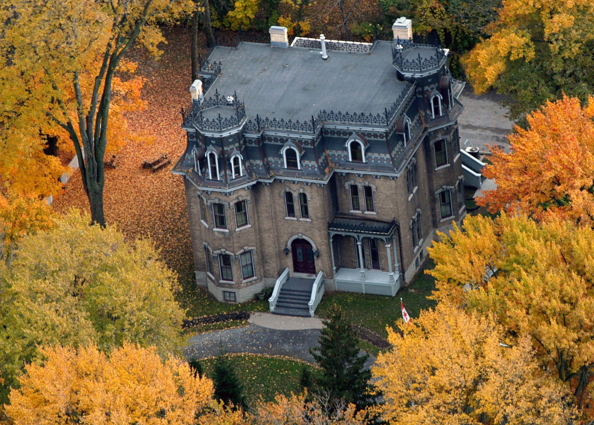 An aerial view of the historic building known as Glanmore National Historic Site during Autumn. The building is surrounded by tall trees in with orange and yellow leaves. ored leaves.