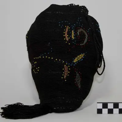A black crocheted Victorian reticule, small drawstring bag, adorned with a pattern of multicolored beads and long tassel.